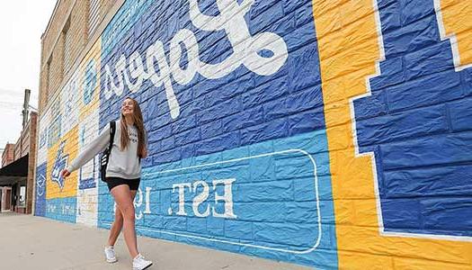 student walking in front of a bet36365体育 theme mural